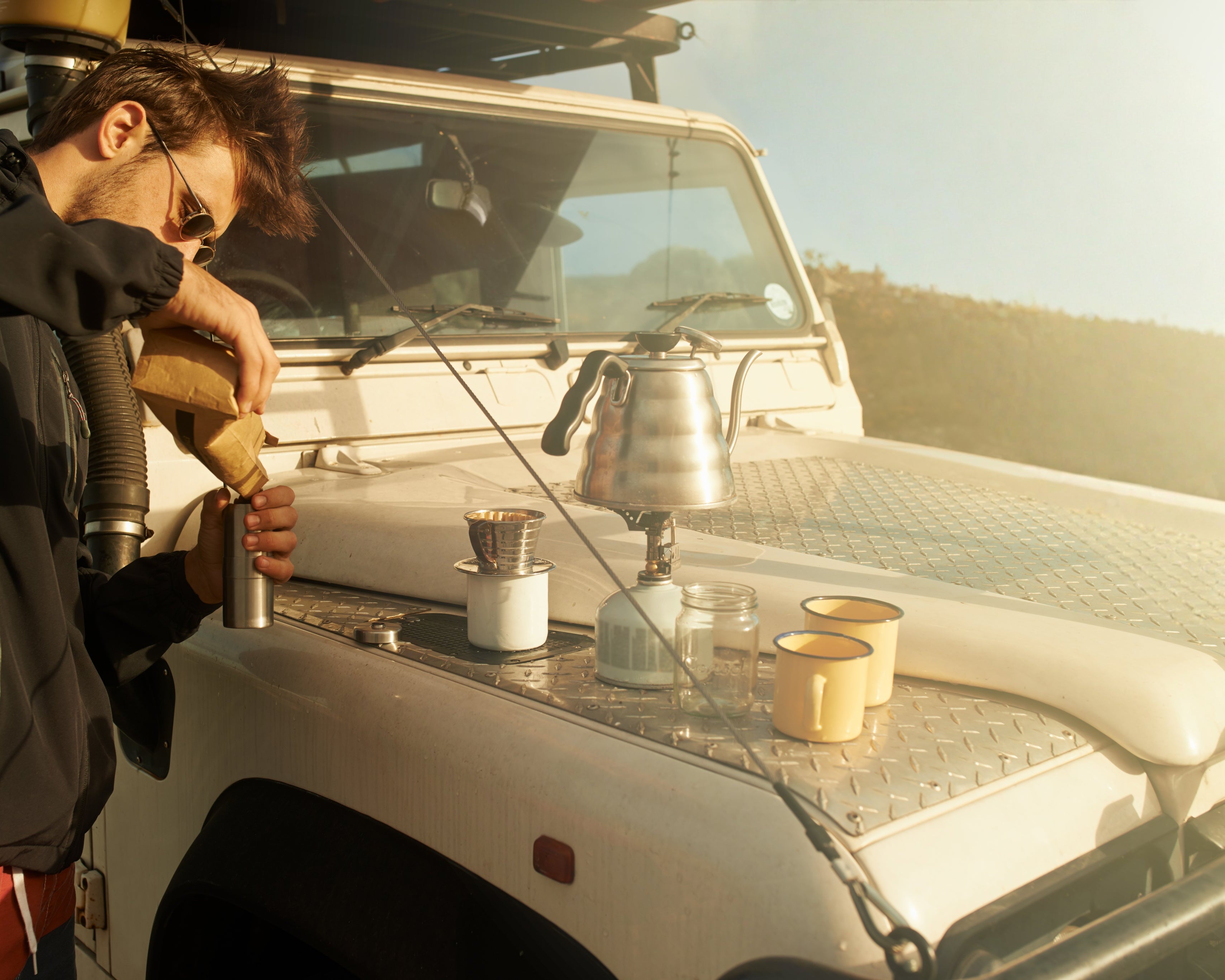 Person preparing coffee on a vehicle with a scenic background